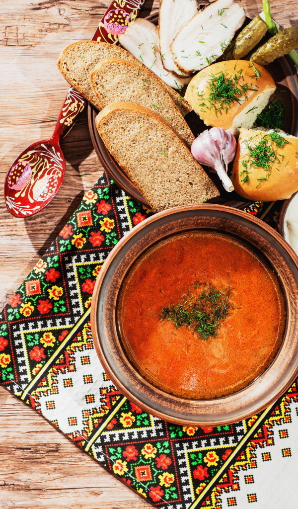 Тарелка борща на столе с салом, хлебом и зеленью