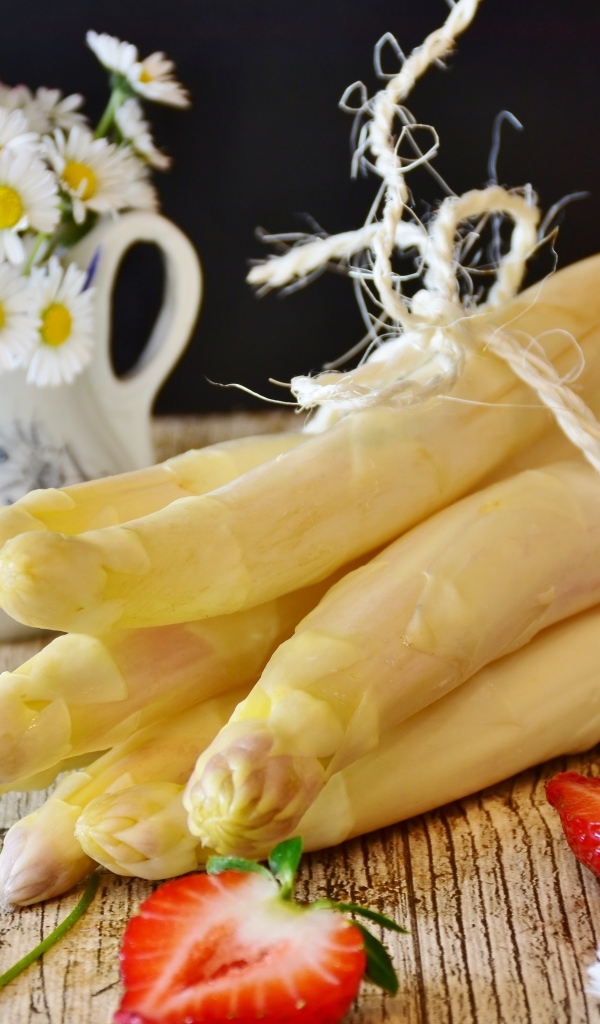 Спаржа на столе с ромашками и ягодами клубники