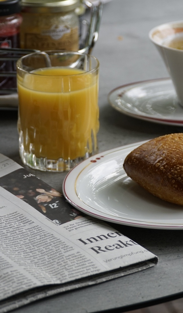 Булочка и стакан сока на столе с газетой