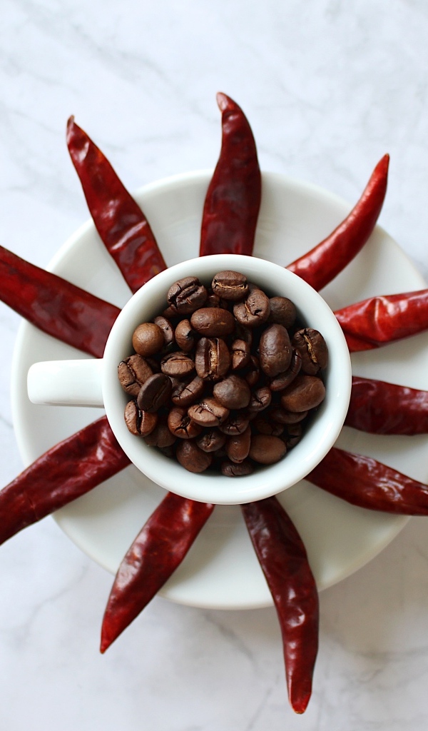 Кофейные зерна в чашке на тарелке с красным перцем
