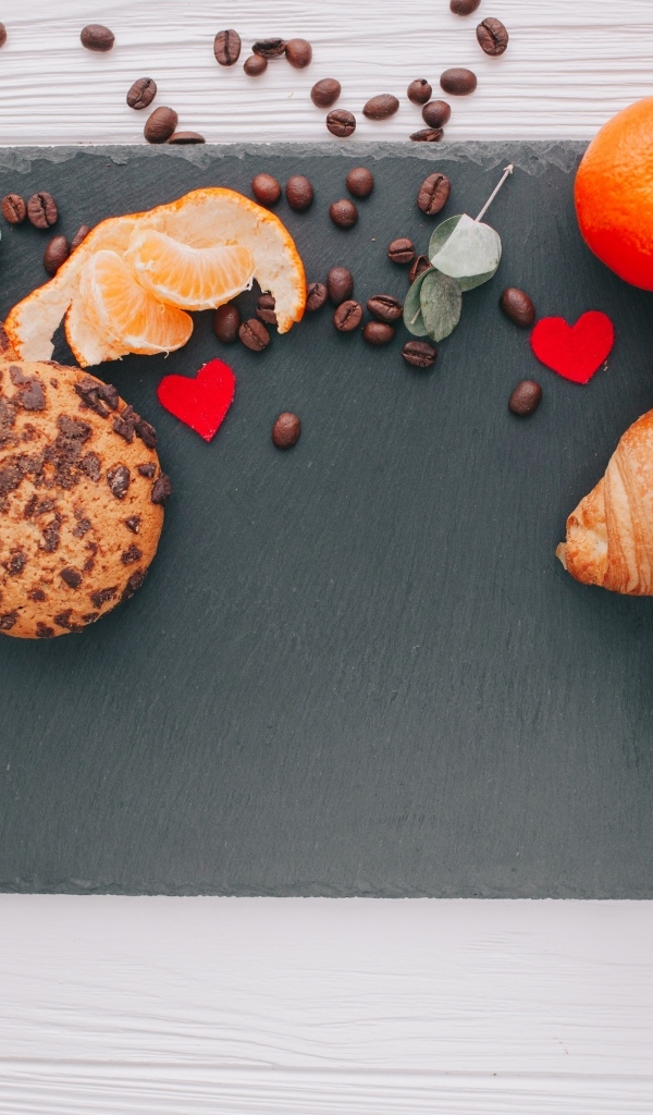 Круассан на столе с печенье, чашкой кофе и мандарином