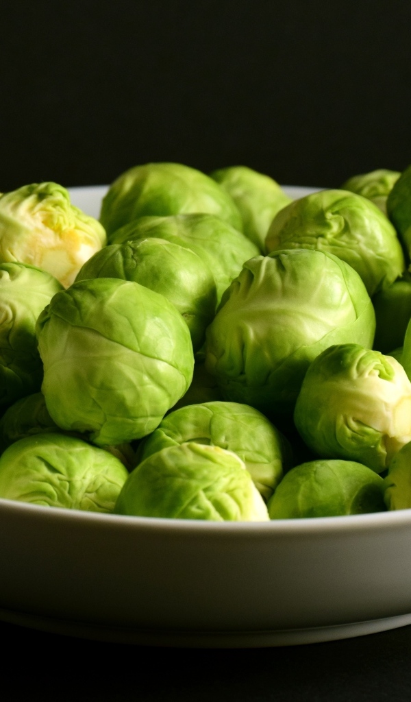 Зеленая брюссельская капуста в тарелке на черном фоне