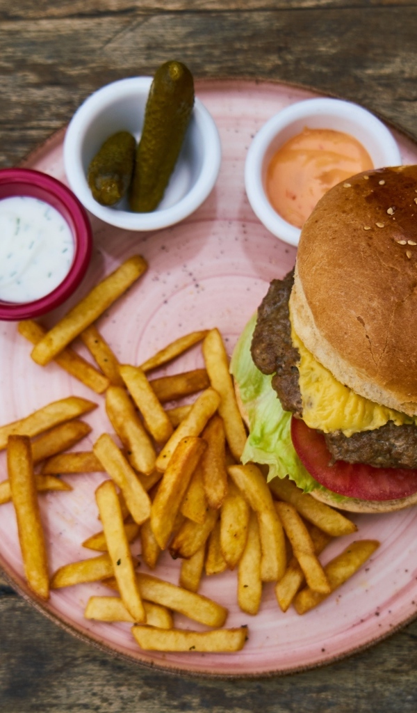 Гамбургер на тарелке с картофелем фри, огурцами и соусом
