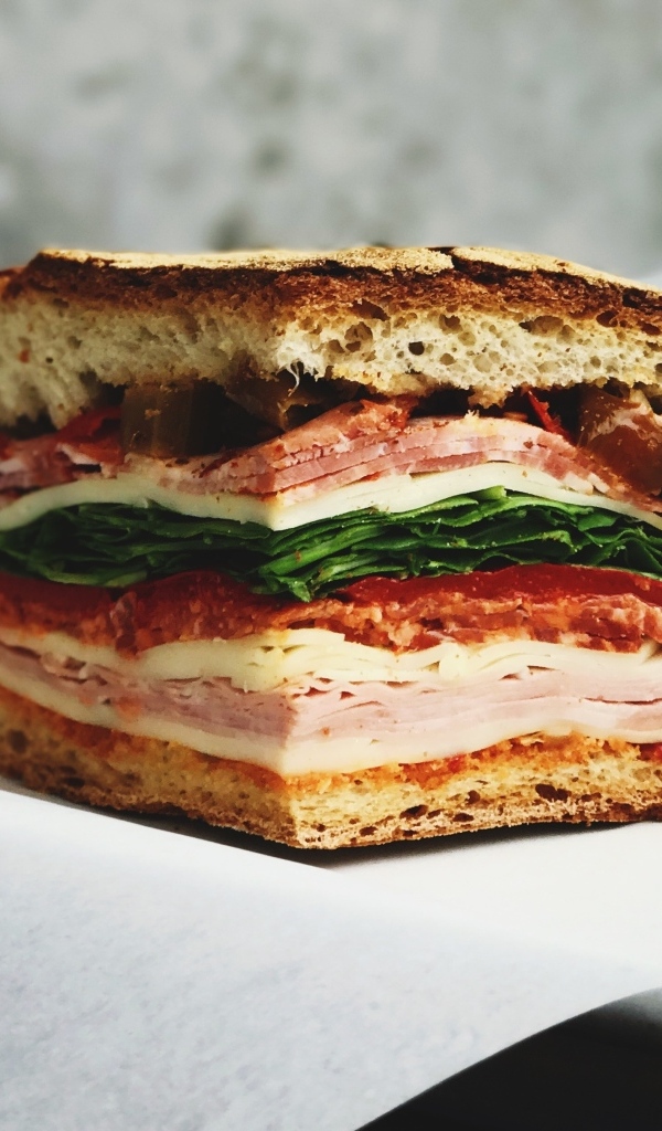 Кусок булки с колбасой, ветчиной и листьями салата