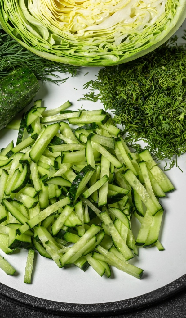 Нарезанные огурцы на столе с капустой и укропом