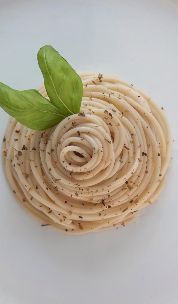 Спагетти с листьями базилика на белой тарелке