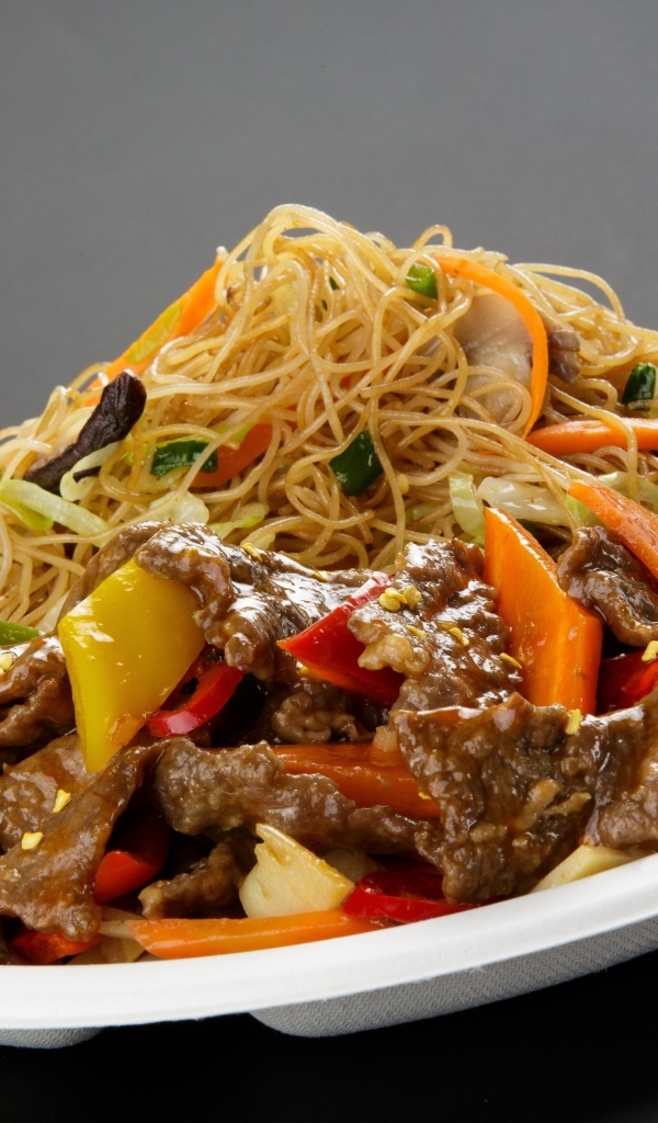 Острая лапша с грибами на белой тарелке на сером фоне