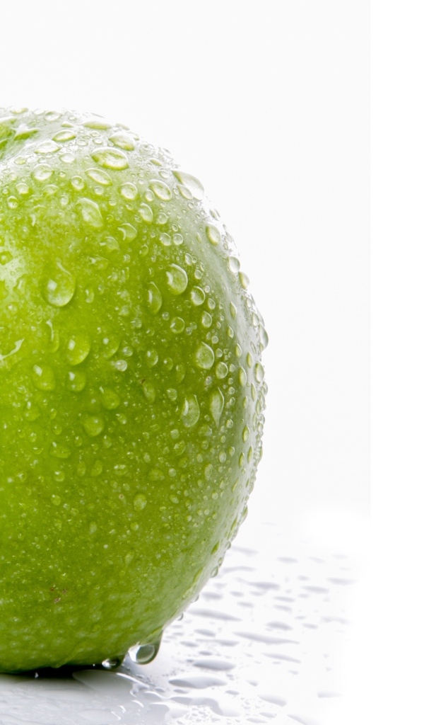 Большое зеленое яблоко в каплях воды на белом фоне