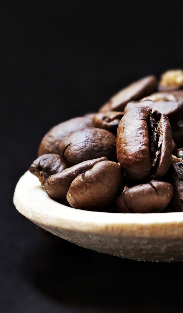 Зерна кофе на деревянной ложке на черном фоне