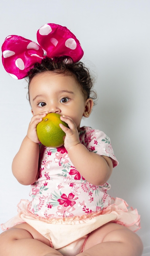 Девочка с большим бантом на голове ест апельсин