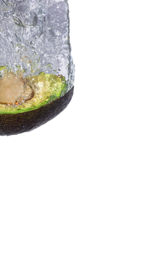 Половина авокадо падает в воду на белом фоне