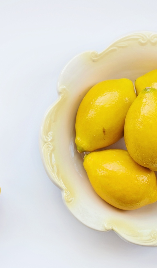 Крупные желтые лимоны в тарелке на белом фоне