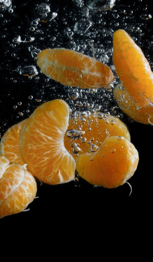 Дольки мандарина в воде на черном фоне