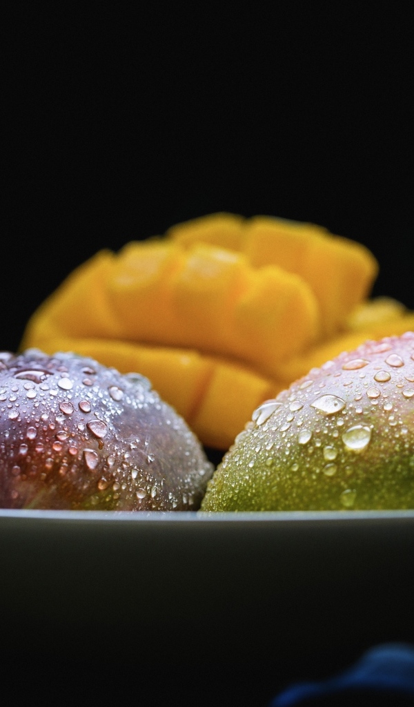 Плоды манго на тарелке на черном фоне