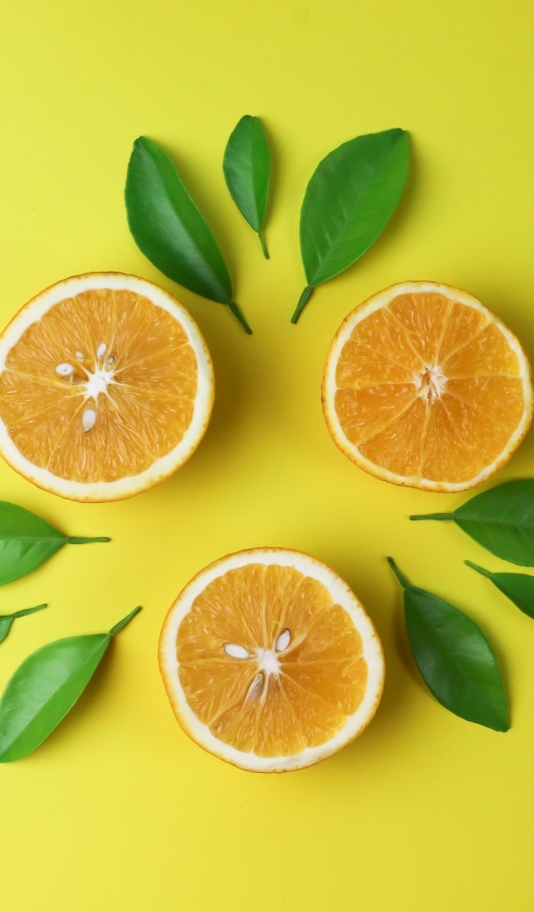 Половинки апельсина с зелеными листьями на желтом фоне