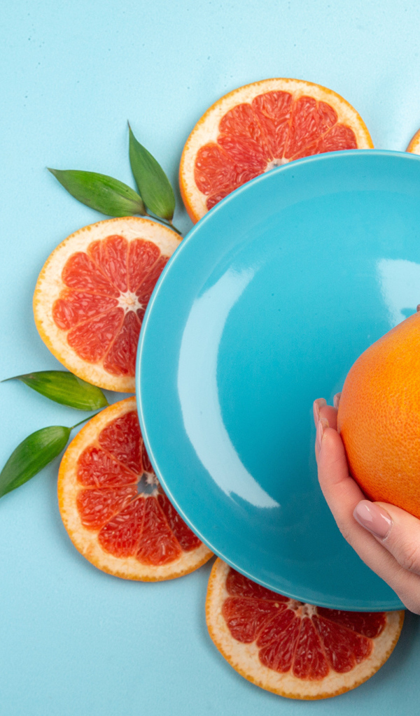 Апельсин в руках девушки на голубом фоне с тарелкой