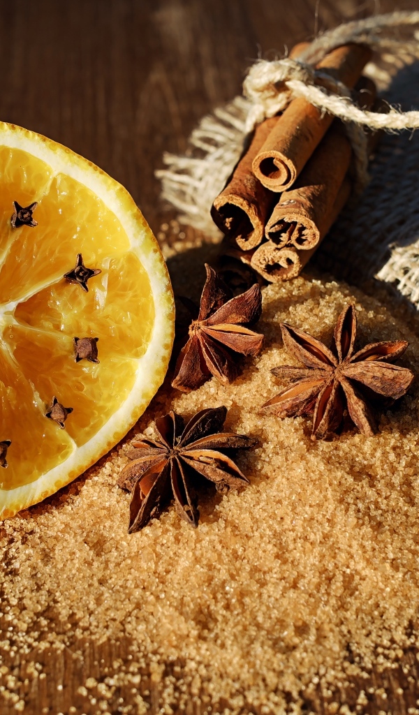 Апельсин с гвоздикой на столе с сахаром, корицей и бадьяном