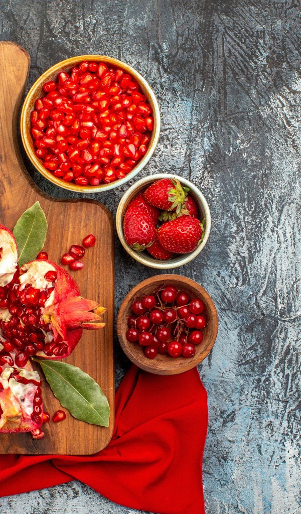 Очищенный гранат на столе с клубникой и ягодами смородины