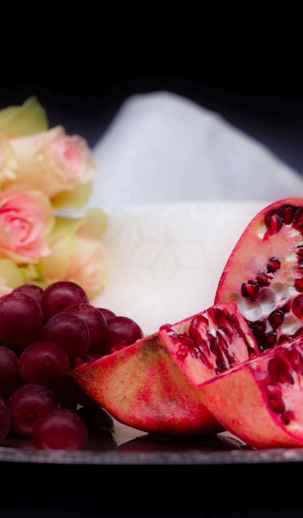 Гранат с виноградом на столе с букетом роз 