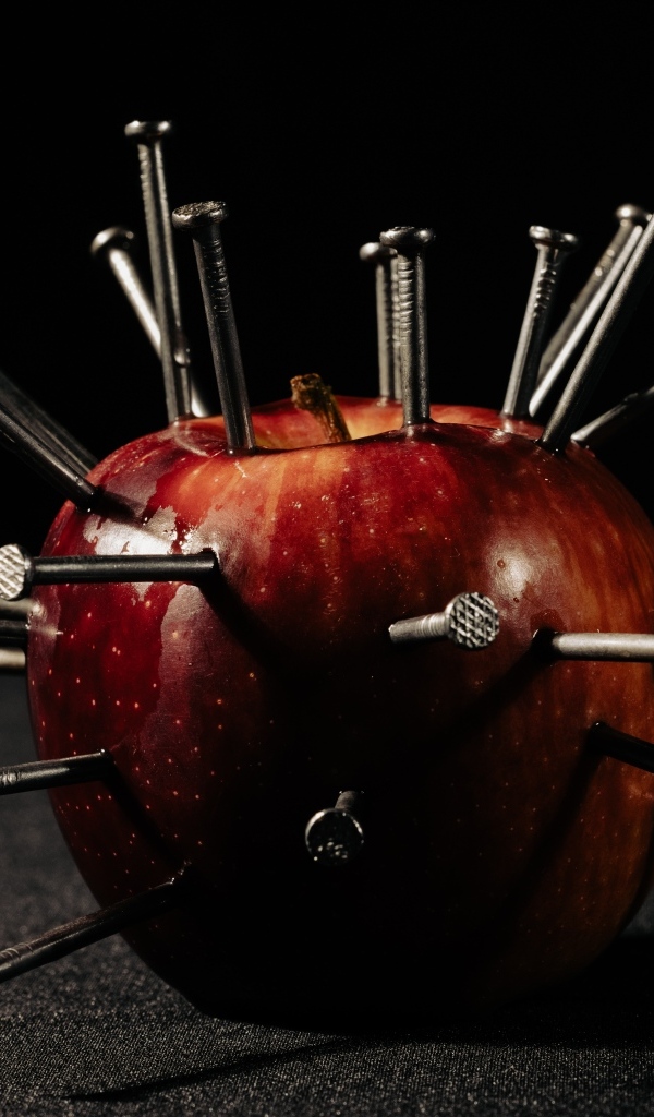 Красное яблоко с гвоздями на черном фоне