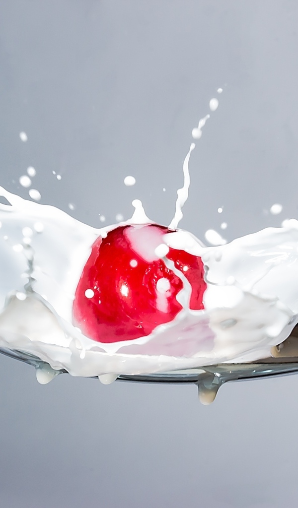 Красная черешня в ложке с молоком на сером фоне