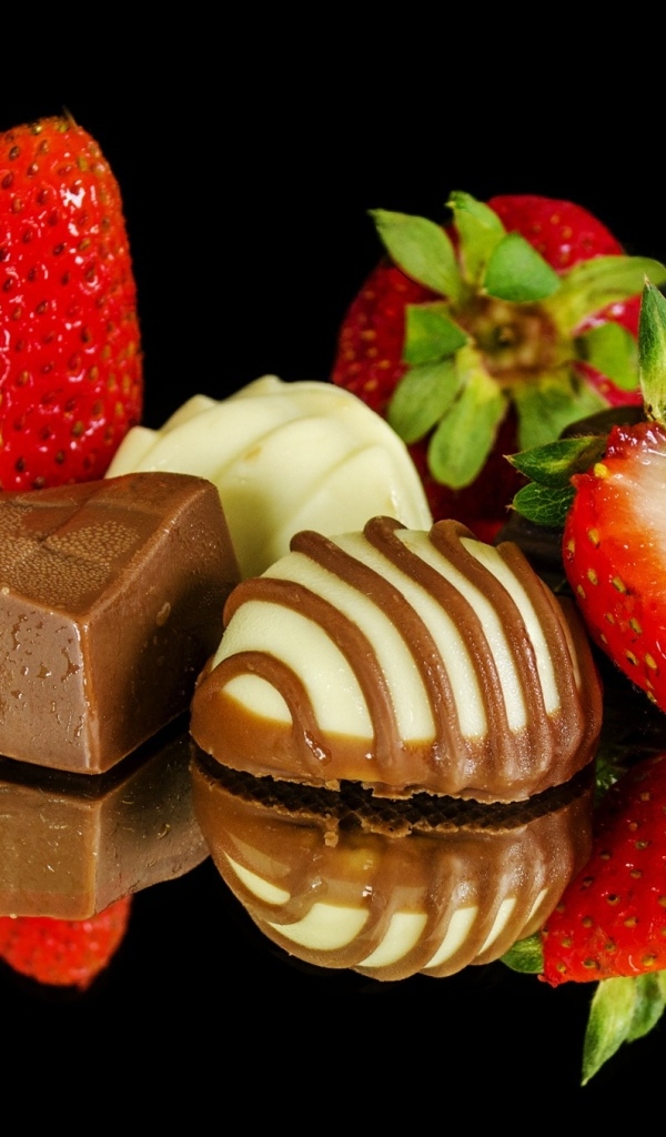 Красная клубника с шоколадными конфетами на черном фоне