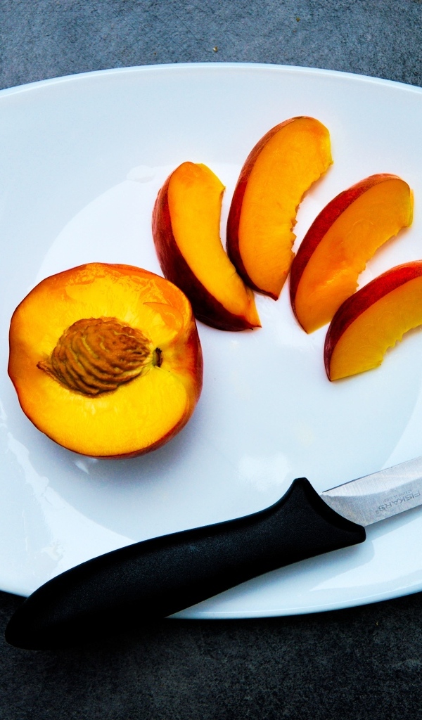 Нарезанный персик на белой тарелке