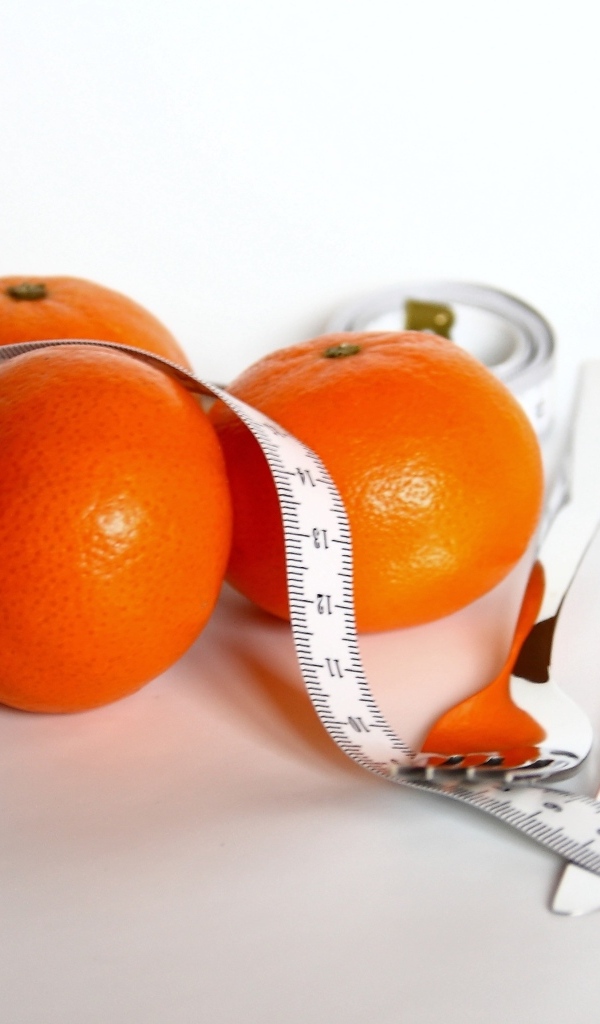 Мандарины с сантиметром и столовыми приборами на белом фоне