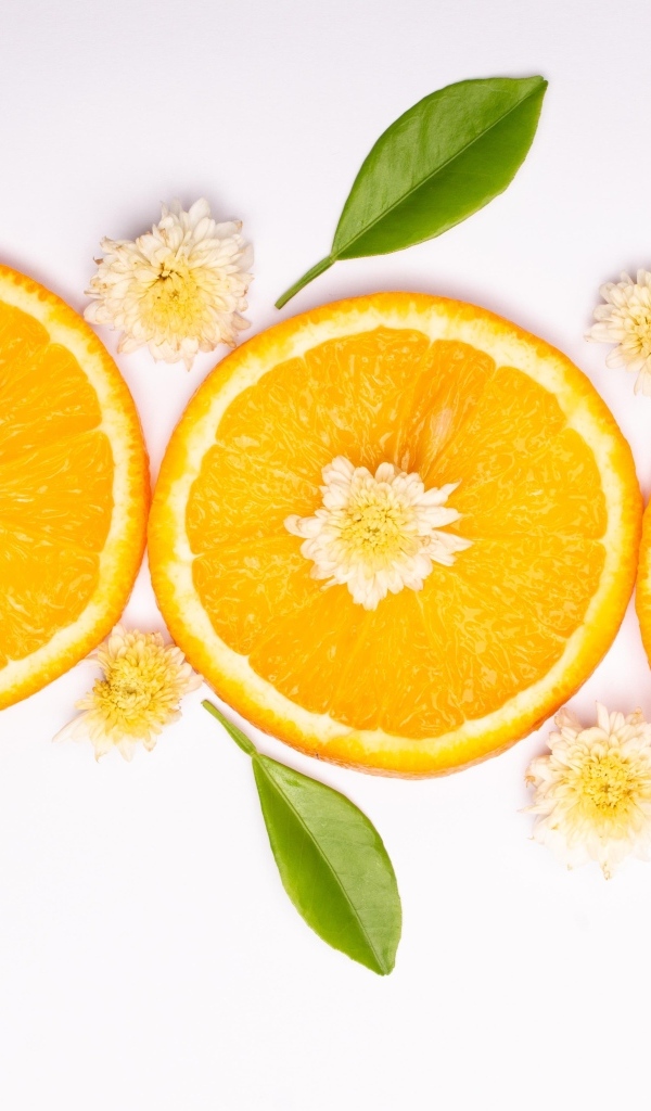 Три кружочка апельсина на белом фоне с цветами и зелеными листьями