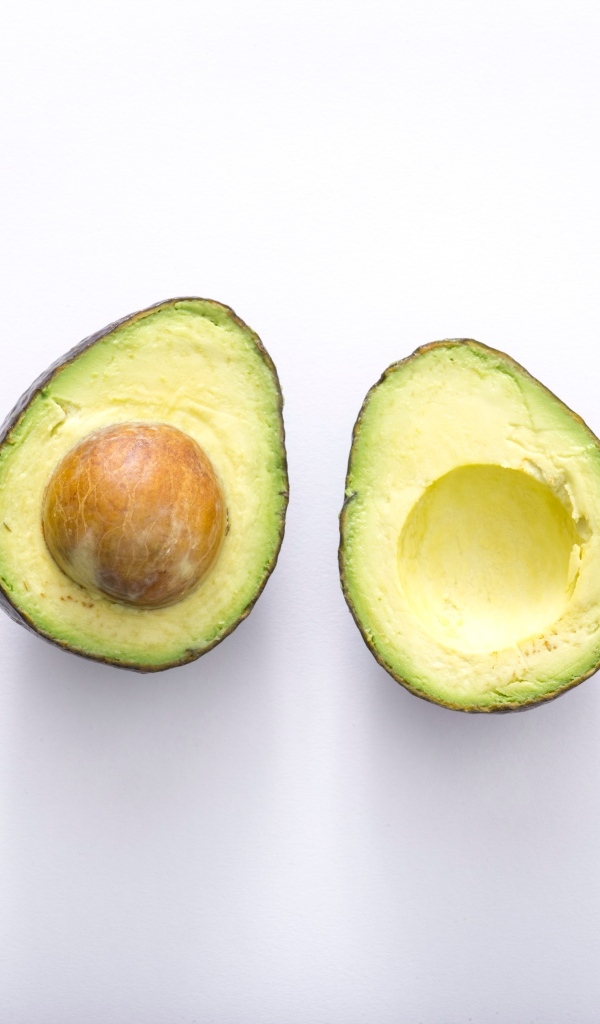 Две половинки зеленого авокадо на сером фоне