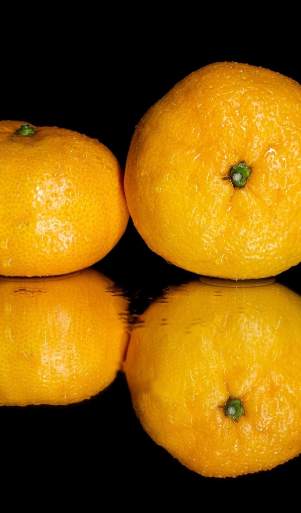 Два мандарина на черной зеркальной поверхности 