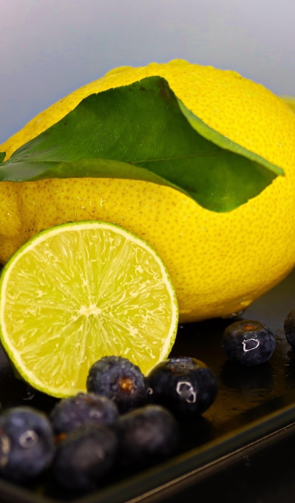 Желтый лимон на тарелке с лаймом и ягодами черники 