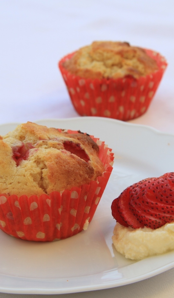 Кекс на большой белой  тарелке с кремом и клубникой