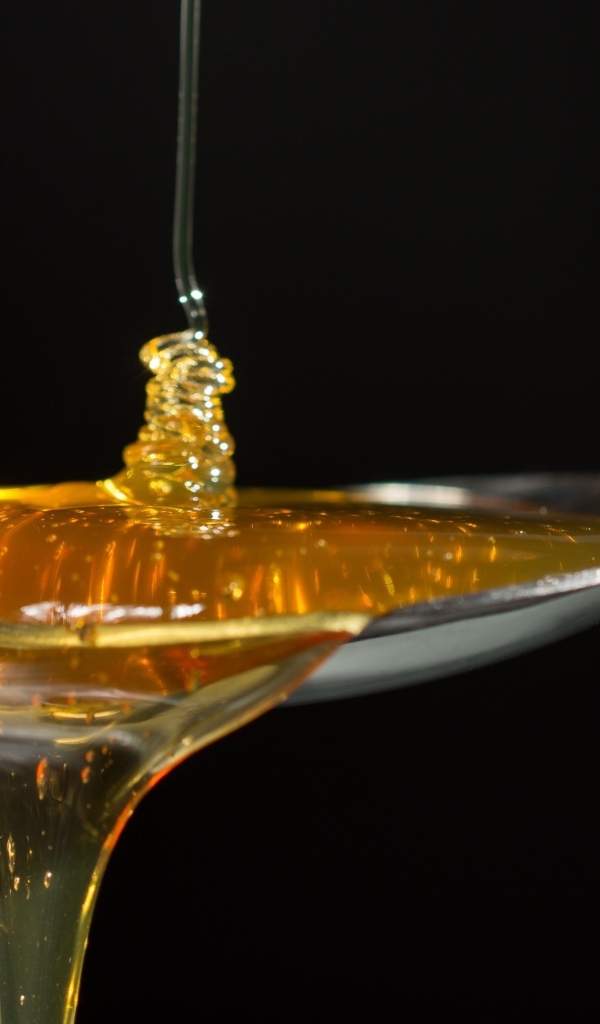 Мед наливают в ложку на черном фоне