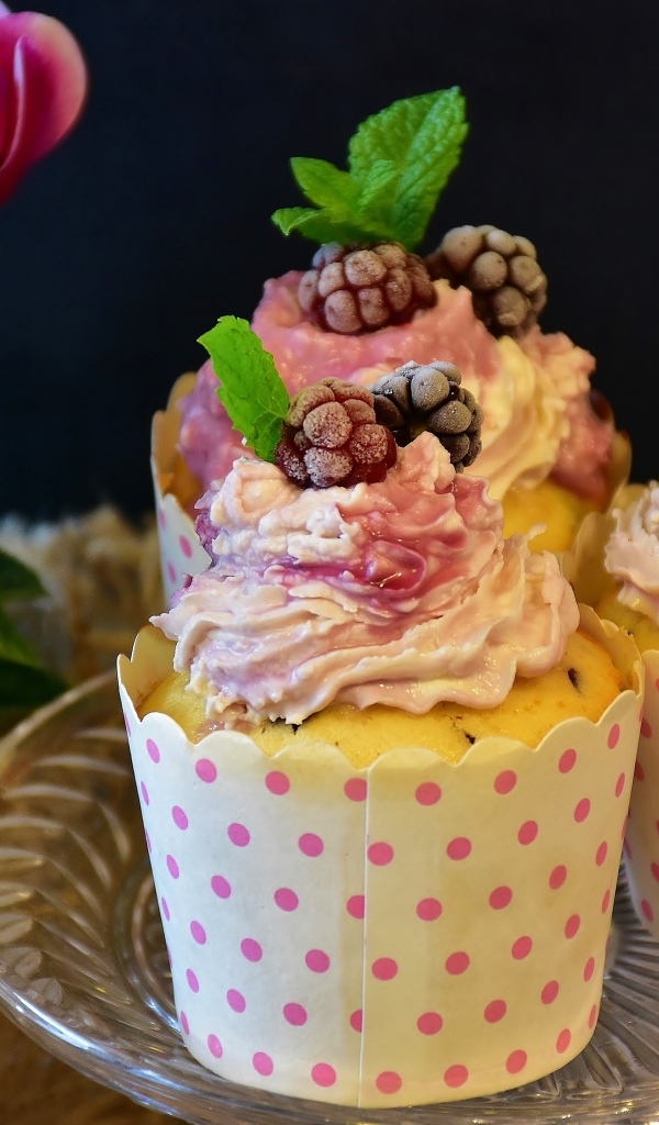 Маффины с кремом и ягодами малины на столе с цветами