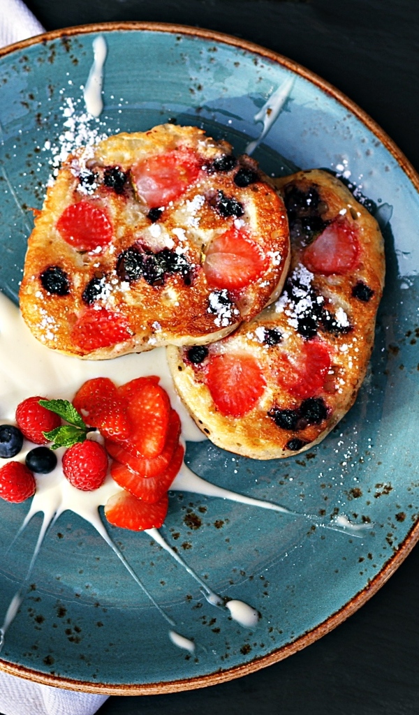 Оладьи на тарелке с ягодами и сметаной