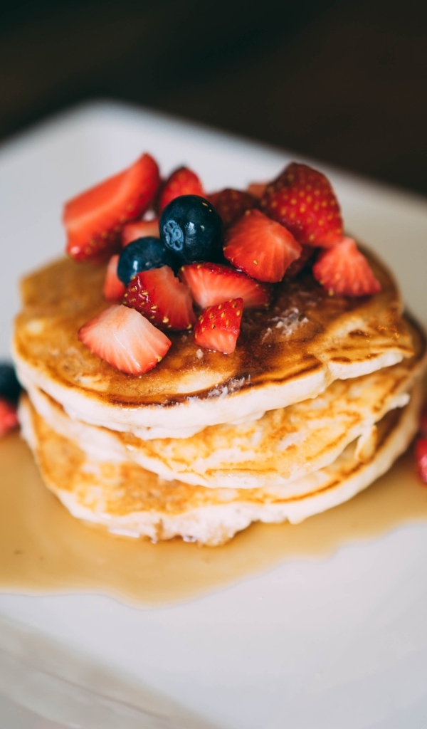 Оладьи с кусочками клубники, медом и черникой на тарелке