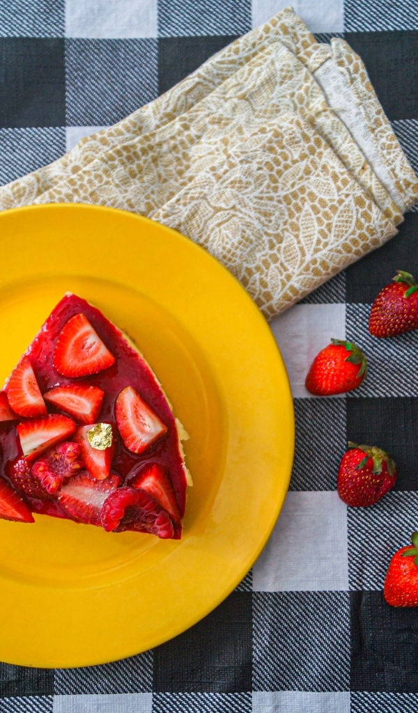 Кусок чизкейка с клубникой на желтой тарелке 