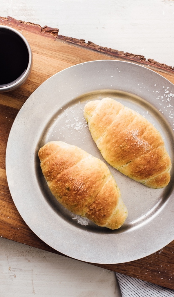 Два круассана на тарелке с чашкой кофе