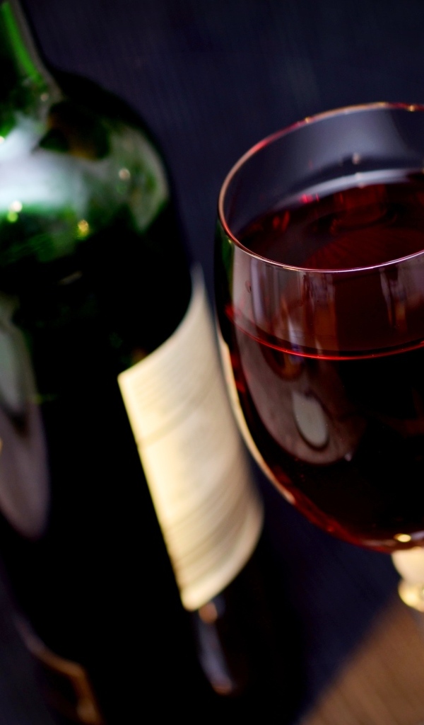 Бутылка красного вина с бокалом на столе