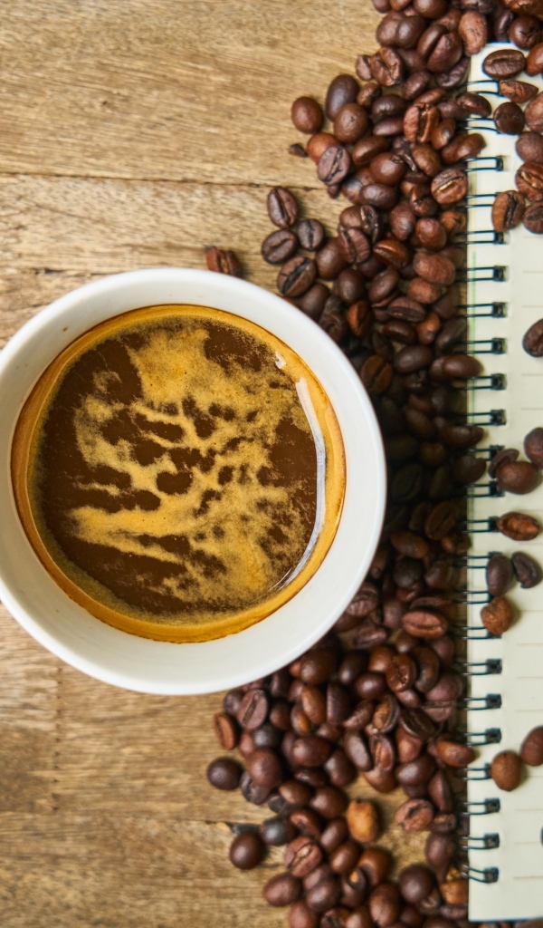 Чашка кофе на столе с зернами и блокнотом