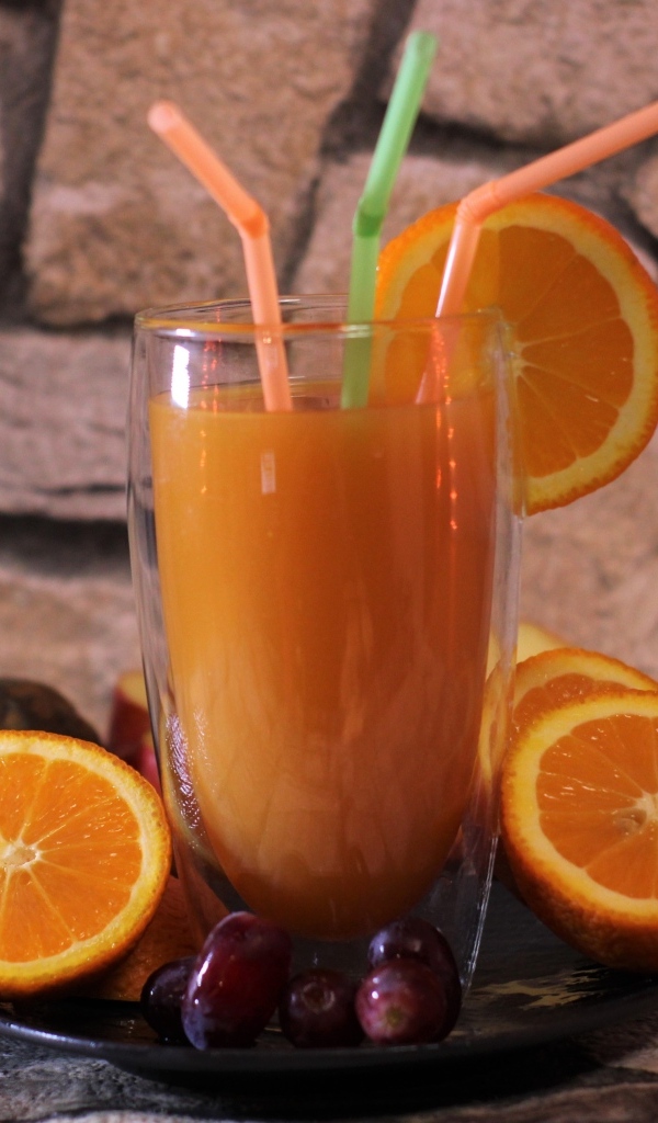 Стакан свежего сока с трубочками на столе с апельсинами