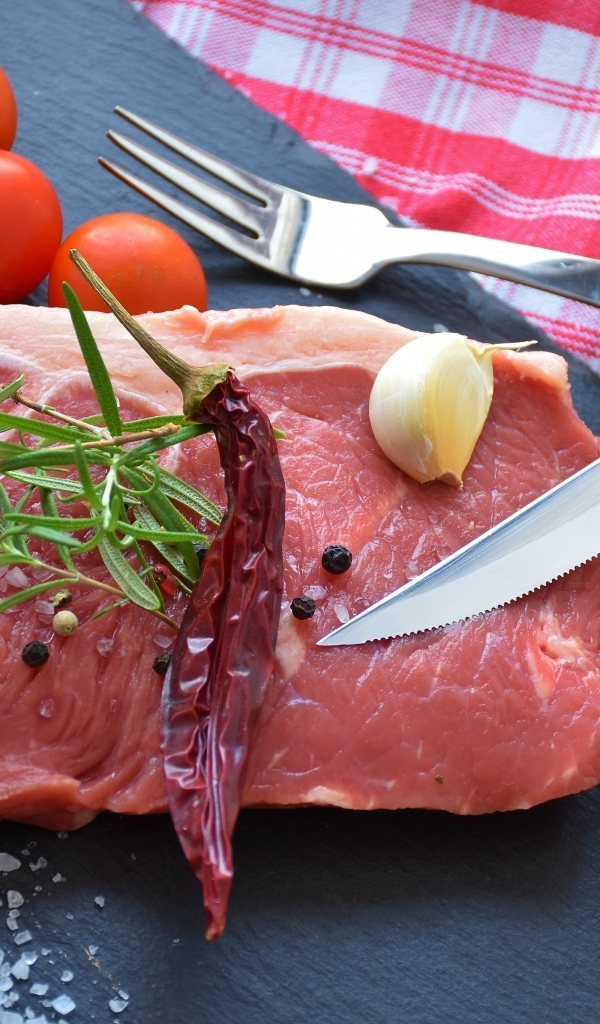 Большой кусок свинины на столе с чесноком и помидорами