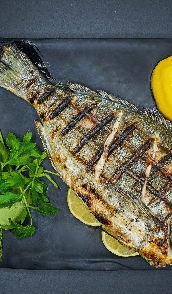 Жареная рыба с лимоном, луком и петрушкой на тарелке