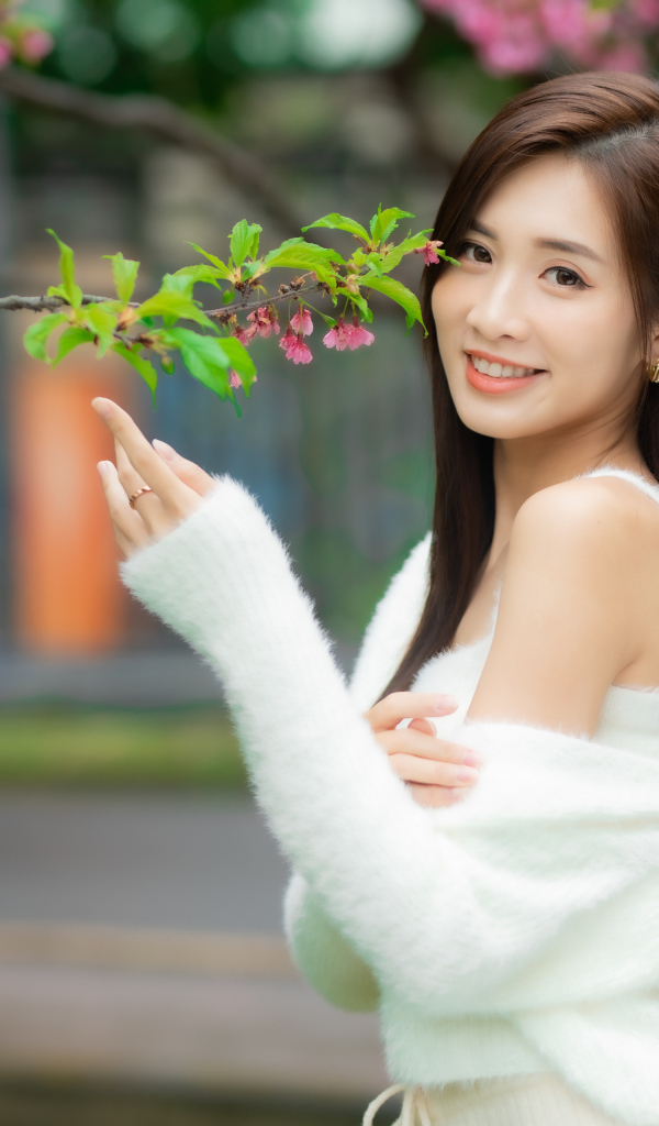 Красивая азиатка в белом свитере стоит у ветки дерева