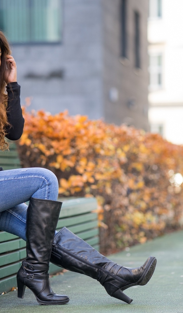 Брюнетка в синих джинсах сидит на лавке