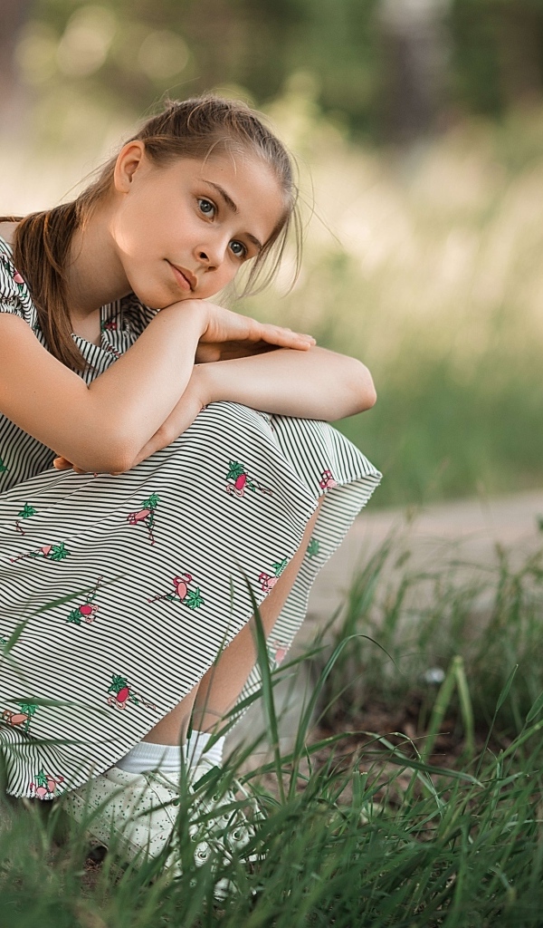 Девушка в платье сидит у зеленой травы