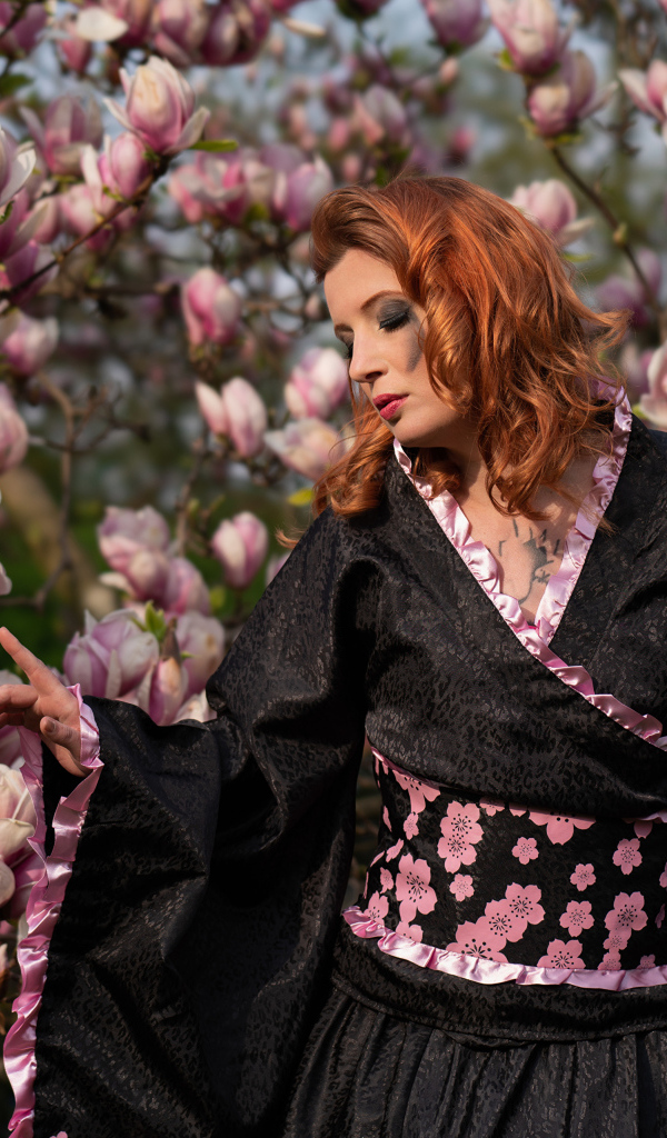 Девушка в кимоно стоит у куста с цветами магнолии