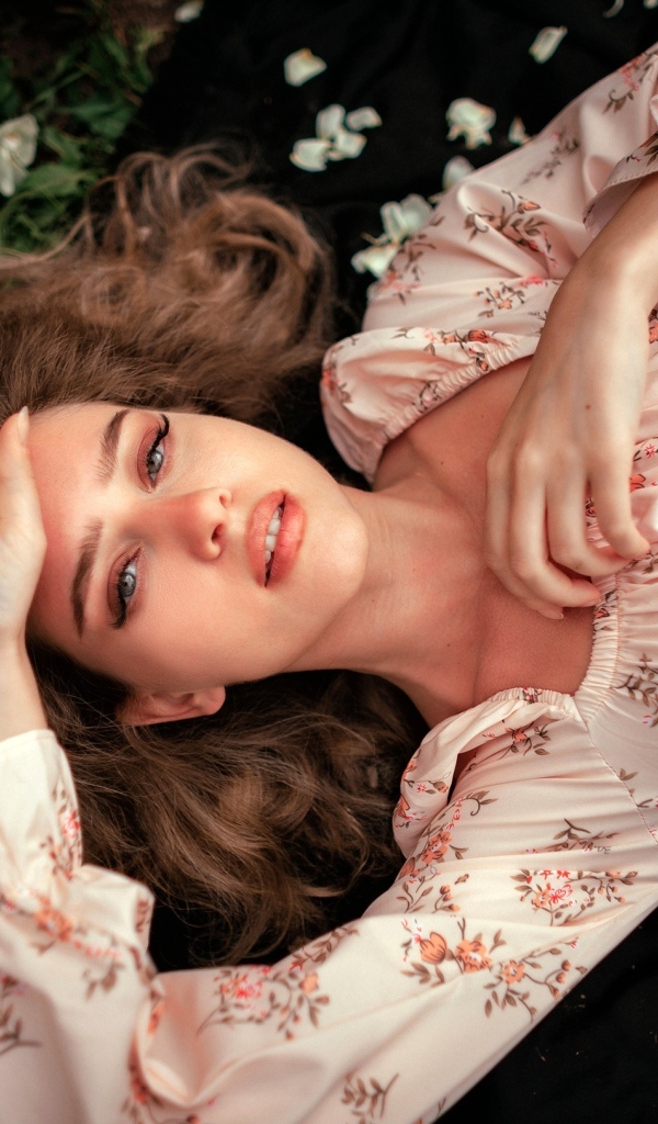 Девушка в розовом платье лежит на земле с цветами розы