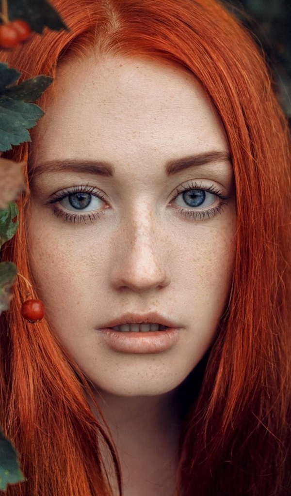 Рыжеволосая девушка стоит у куста с боярышником